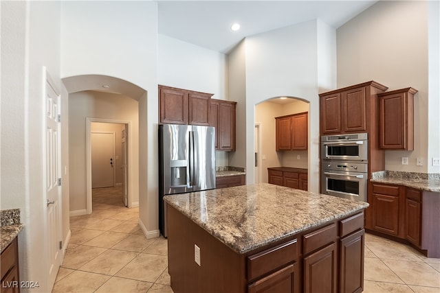 kitchen with light stone counters, light tile patterned floors, a kitchen island, stainless steel appliances, and a high ceiling