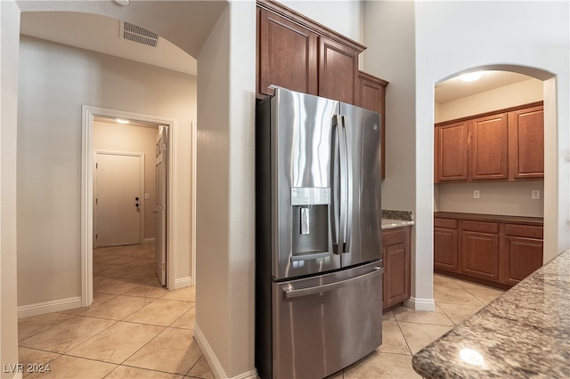 kitchen with dark stone countertops, stainless steel fridge, and light tile patterned floors