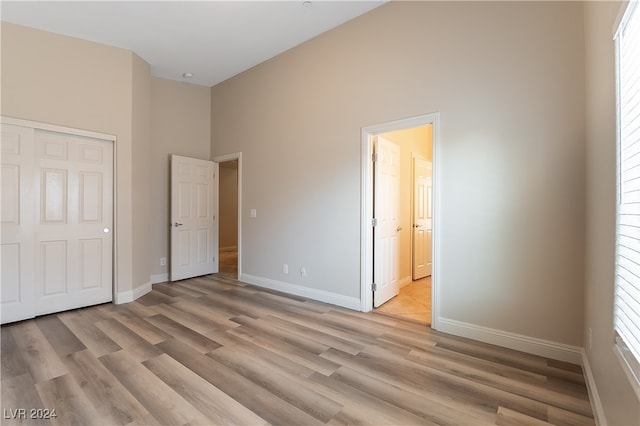 unfurnished bedroom featuring a high ceiling, a closet, and light hardwood / wood-style flooring