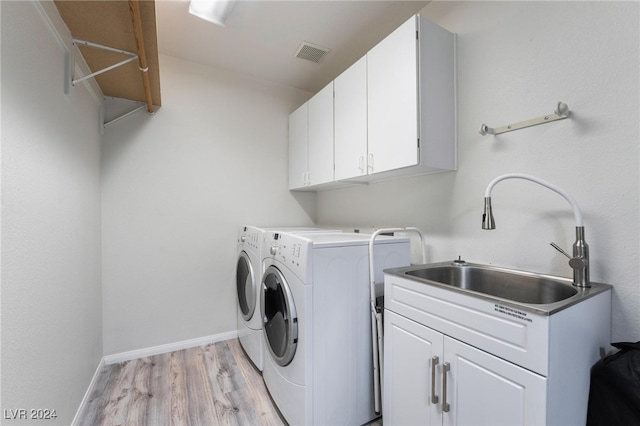 laundry area with light hardwood / wood-style floors, washer and dryer, cabinets, and sink