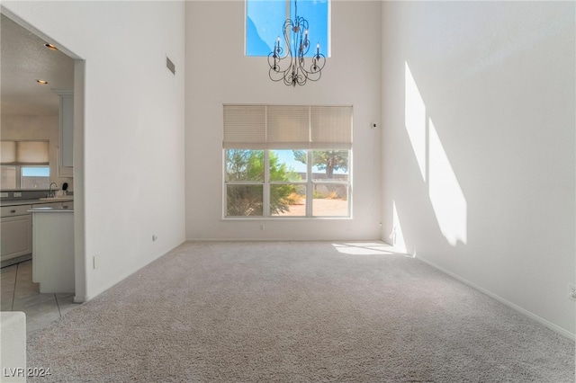 unfurnished living room featuring light colored carpet, sink, a chandelier, and a high ceiling