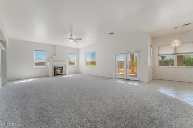 unfurnished living room featuring french doors, plenty of natural light, ceiling fan with notable chandelier, and light tile patterned floors