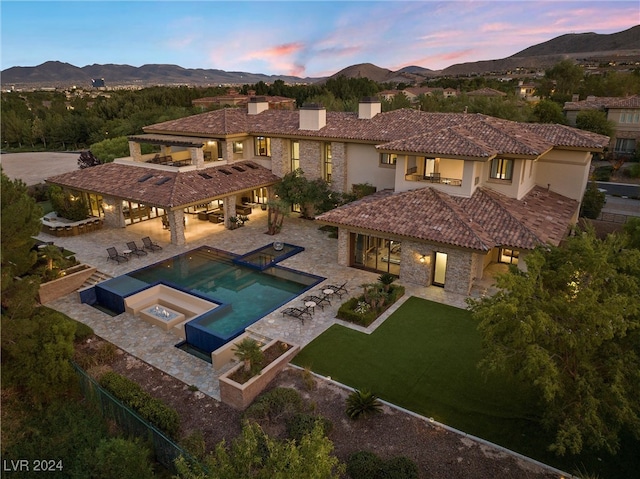 back house at dusk with a yard, a mountain view, a patio, and a pool with hot tub