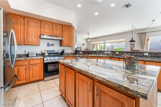 kitchen with ceiling fan, light tile patterned floors, appliances with stainless steel finishes, a center island, and dark stone countertops