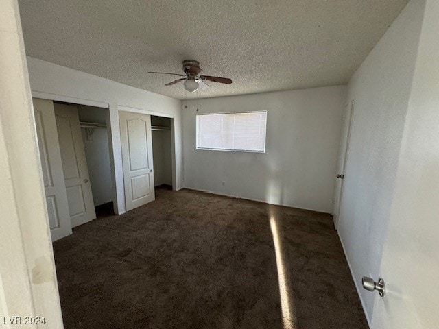 unfurnished bedroom featuring ceiling fan, multiple closets, a textured ceiling, and dark colored carpet