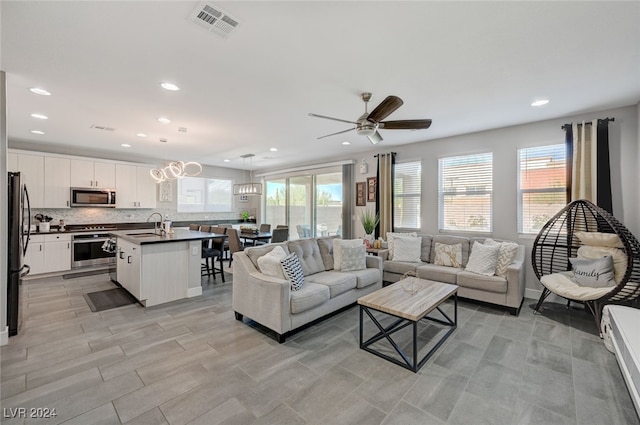 living room with ceiling fan with notable chandelier, sink, and a healthy amount of sunlight