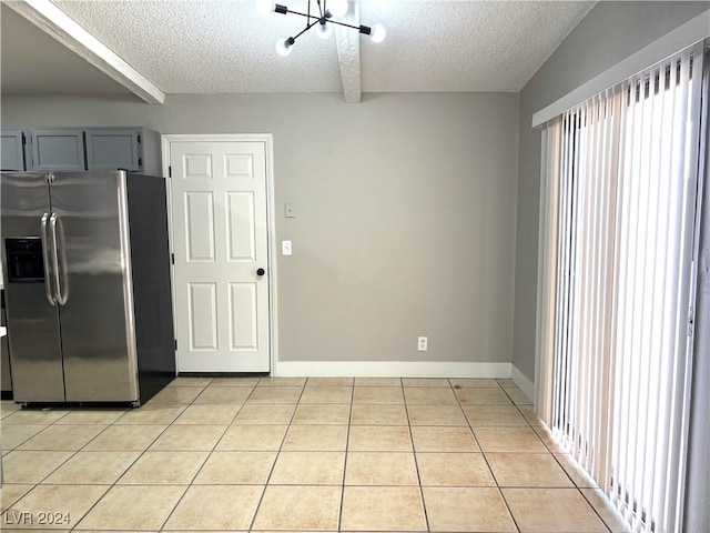 kitchen featuring stainless steel fridge, light tile patterned floors, beam ceiling, gray cabinetry, and a textured ceiling