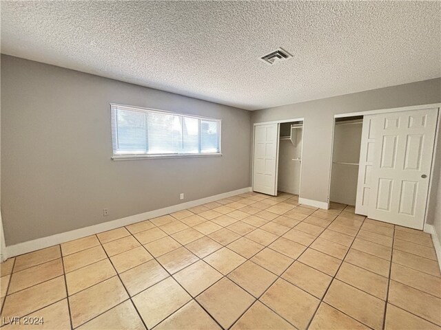 unfurnished bedroom with light tile patterned flooring, two closets, and a textured ceiling