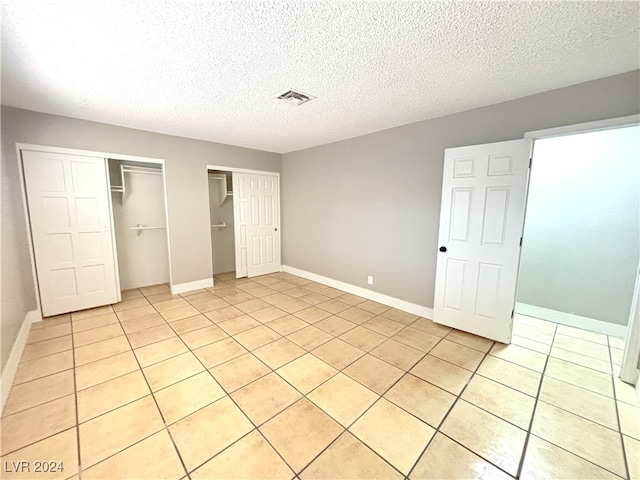 unfurnished bedroom featuring multiple closets, light tile patterned floors, and a textured ceiling