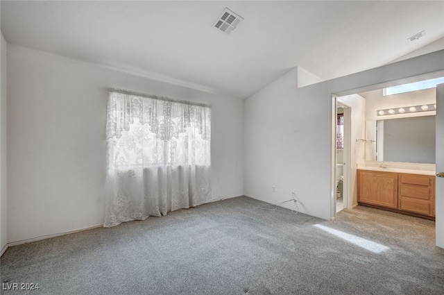 unfurnished bedroom with light colored carpet, lofted ceiling, and ensuite bath