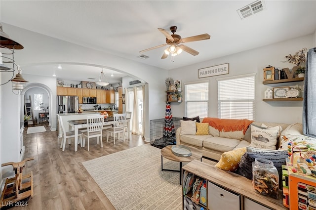 living room featuring arched walkways, light wood-type flooring, visible vents, and a ceiling fan