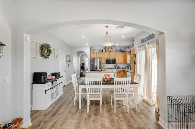 dining space with arched walkways, visible vents, light wood-style flooring, and baseboards