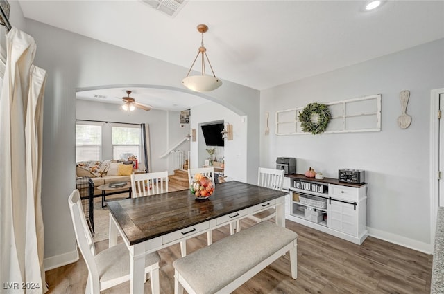 dining space with arched walkways, wood finished floors, a ceiling fan, baseboards, and stairway