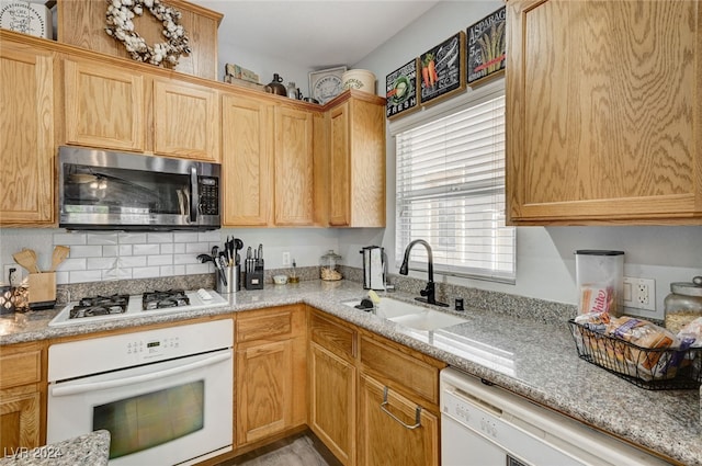 kitchen featuring light stone counters, white appliances, a sink, and decorative backsplash