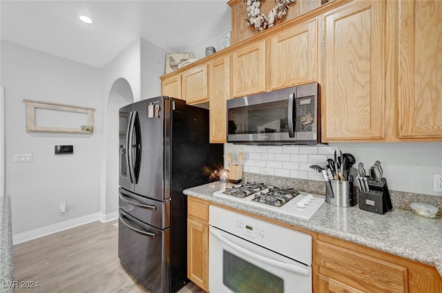 kitchen with arched walkways, light wood finished floors, stainless steel appliances, light brown cabinetry, and light stone countertops