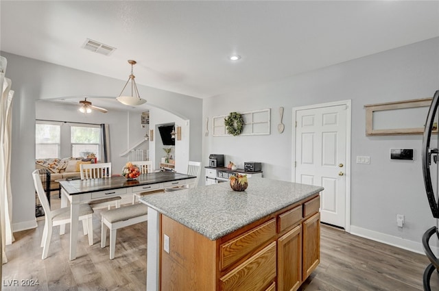 kitchen with visible vents, arched walkways, wood finished floors, a center island, and decorative light fixtures