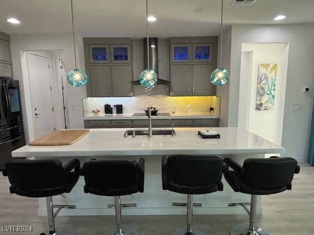 kitchen featuring a kitchen bar, pendant lighting, black appliances, and wall chimney exhaust hood