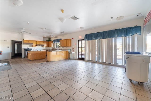 kitchen featuring light tile patterned flooring, a kitchen island, a wealth of natural light, and stainless steel stove