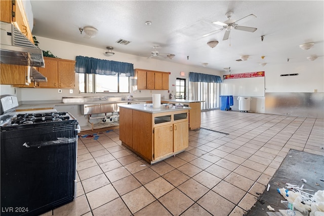 kitchen featuring ceiling fan, a center island, gas stove, range hood, and light tile patterned floors