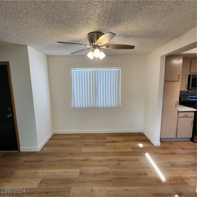 unfurnished dining area with light wood-type flooring, ceiling fan, and a textured ceiling