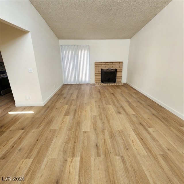 unfurnished living room with a brick fireplace, light hardwood / wood-style floors, and a textured ceiling