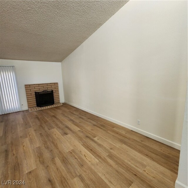 unfurnished living room featuring a fireplace, light hardwood / wood-style floors, vaulted ceiling, and a textured ceiling