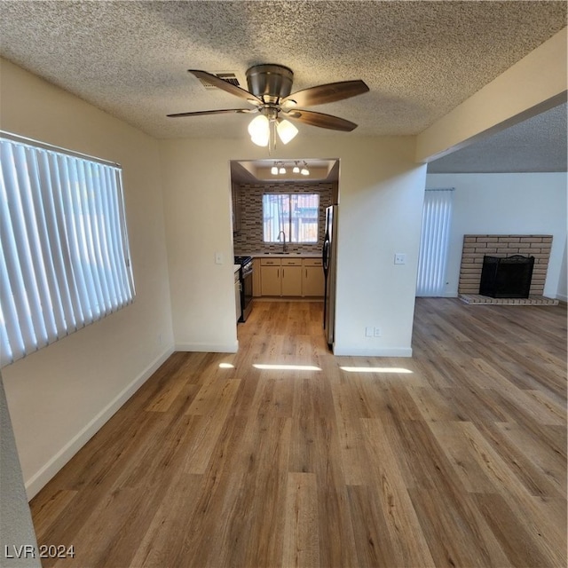 unfurnished living room with ceiling fan, sink, a fireplace, light hardwood / wood-style flooring, and a textured ceiling