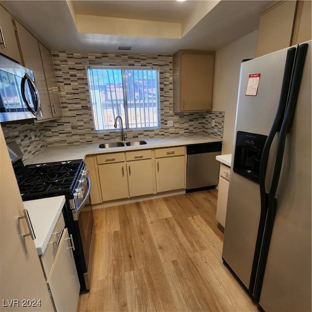 kitchen featuring a raised ceiling, sink, tasteful backsplash, light hardwood / wood-style flooring, and stainless steel appliances