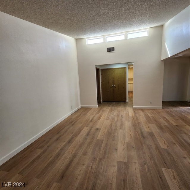 empty room with wood-type flooring, a high ceiling, and a textured ceiling