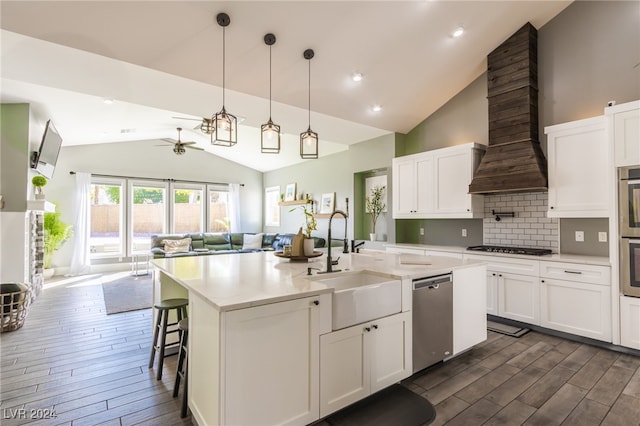 kitchen with custom range hood, decorative light fixtures, a center island with sink, sink, and dishwasher