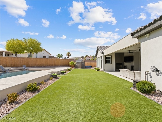 view of yard featuring ceiling fan, a fenced in pool, a storage unit, and a patio area