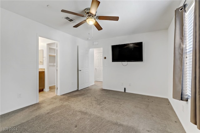 unfurnished bedroom with ensuite bathroom, ceiling fan, light carpet, and a spacious closet