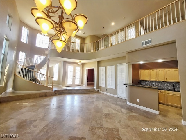 unfurnished living room featuring a high ceiling, a notable chandelier, french doors, and sink