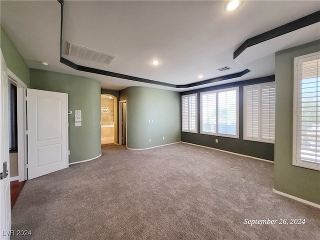 unfurnished bedroom with ensuite bathroom, a tray ceiling, and carpet floors