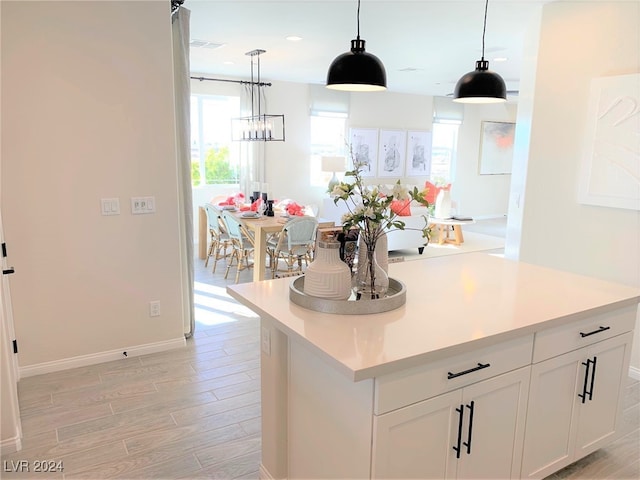 kitchen featuring white cabinets, hanging light fixtures, a kitchen island, a chandelier, and light hardwood / wood-style floors