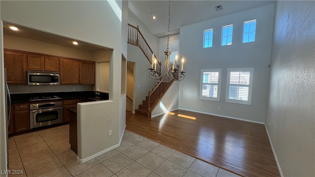 kitchen featuring a high ceiling, light hardwood / wood-style floors, an inviting chandelier, and stainless steel appliances