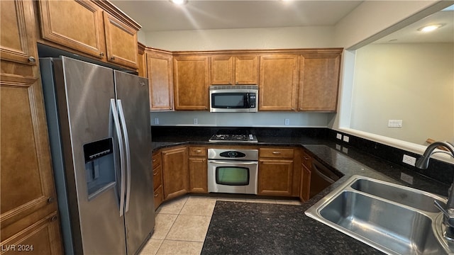 kitchen with appliances with stainless steel finishes, dark stone countertops, sink, and light tile patterned floors