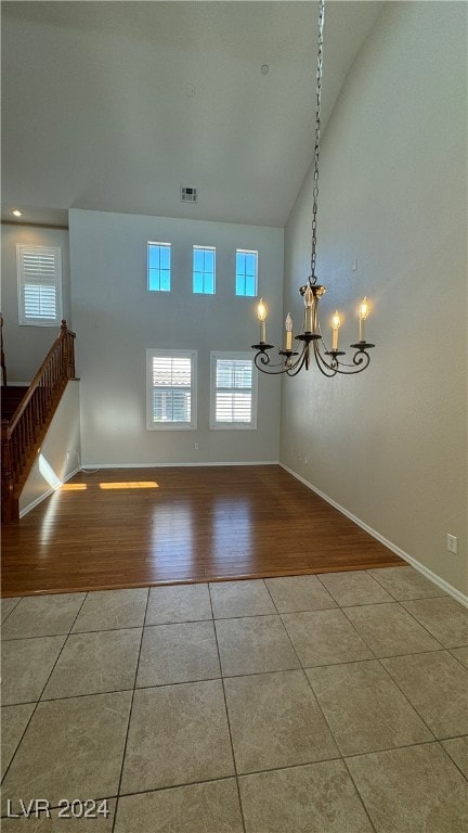 empty room featuring a notable chandelier, high vaulted ceiling, and light hardwood / wood-style flooring