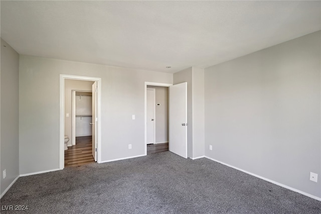 unfurnished bedroom featuring a closet, a walk in closet, and dark colored carpet