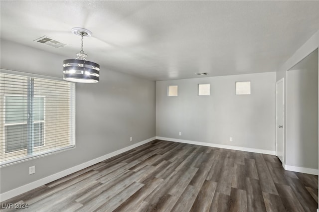 unfurnished room featuring a textured ceiling, dark hardwood / wood-style floors, and an inviting chandelier