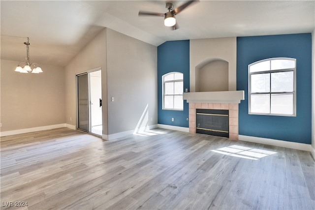 unfurnished living room featuring vaulted ceiling, light hardwood / wood-style flooring, a healthy amount of sunlight, and a tiled fireplace