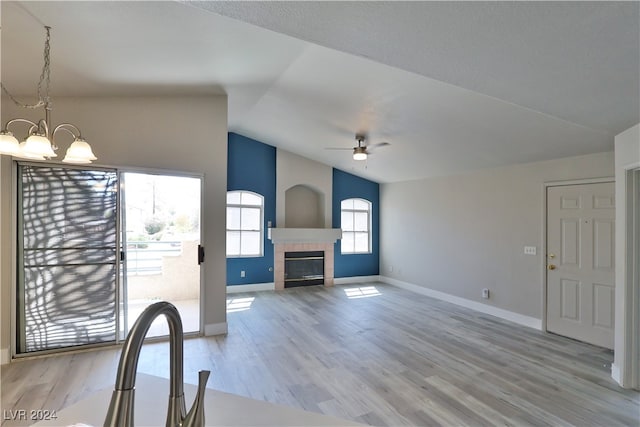 unfurnished living room with ceiling fan with notable chandelier, light hardwood / wood-style floors, a tile fireplace, and vaulted ceiling