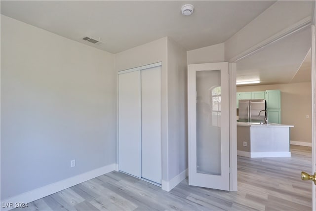 unfurnished bedroom featuring stainless steel fridge, a closet, light hardwood / wood-style floors, and sink