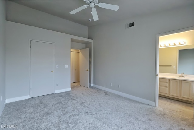 unfurnished bedroom featuring light carpet, ensuite bathroom, ceiling fan, sink, and a closet