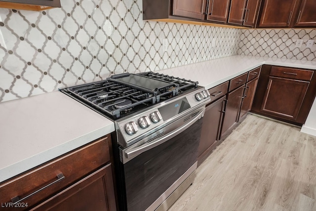 kitchen with stainless steel gas stove, dark brown cabinetry, tasteful backsplash, and light wood-type flooring