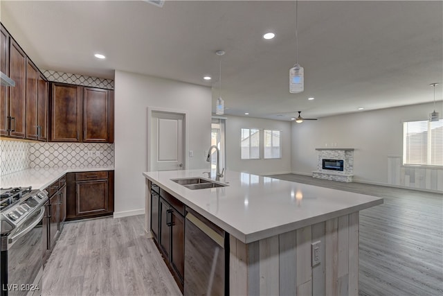 kitchen with appliances with stainless steel finishes, decorative light fixtures, sink, and light hardwood / wood-style flooring