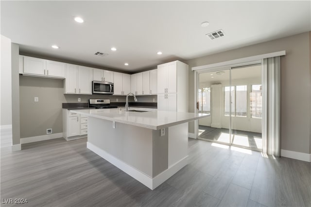 kitchen with stove, sink, light wood-type flooring, an island with sink, and white cabinetry