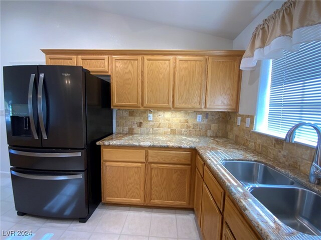 kitchen with lofted ceiling, light tile patterned floors, sink, backsplash, and black refrigerator with ice dispenser