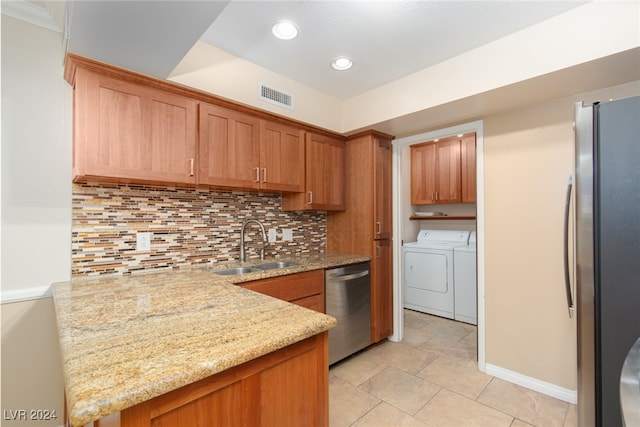 kitchen with tasteful backsplash, washing machine and clothes dryer, sink, light stone counters, and stainless steel appliances