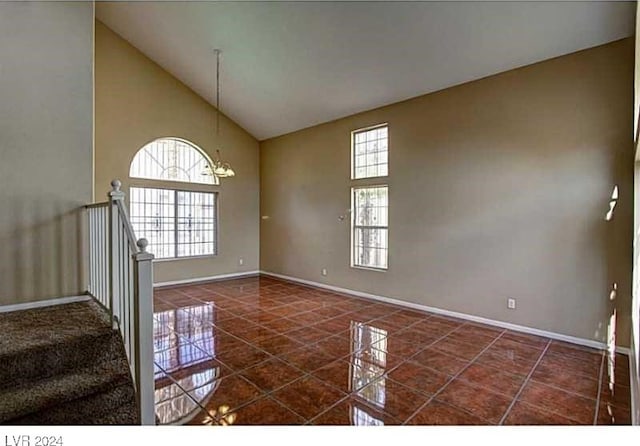 spare room with a notable chandelier, dark tile patterned floors, and high vaulted ceiling